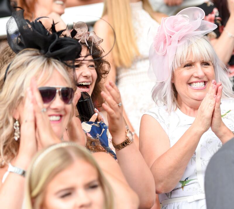 Ladies dressed for the races smile and clap in the crowd