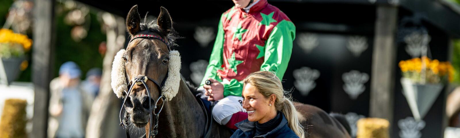 A groom leading a racehorse and jockey through the parade ring at Lingfield Park Racecourse