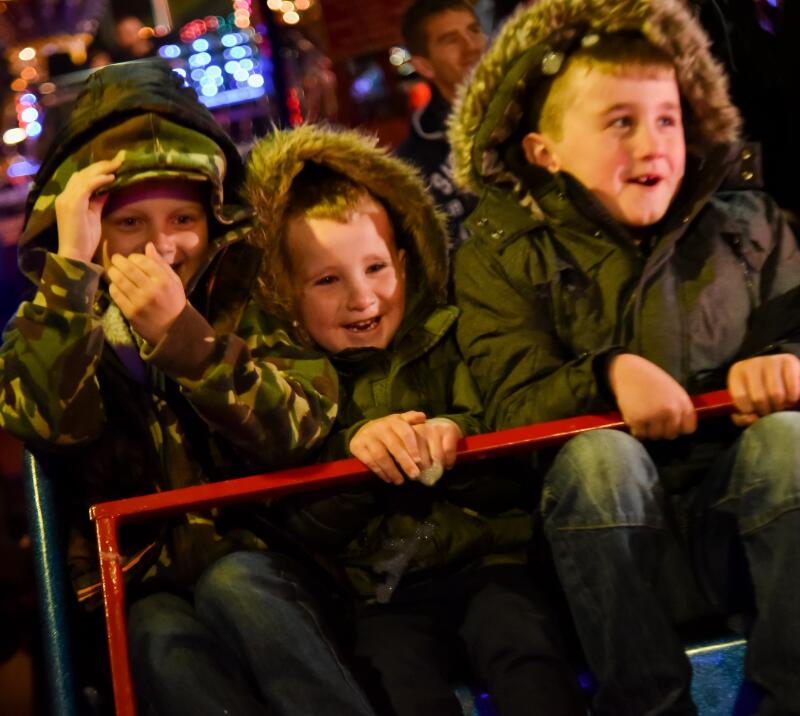 Three boys laughing and enjoying a fair ground ride at a bonfire night event