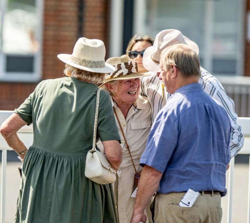 A group of racegoers in sun hats at Lingfield Park embrace