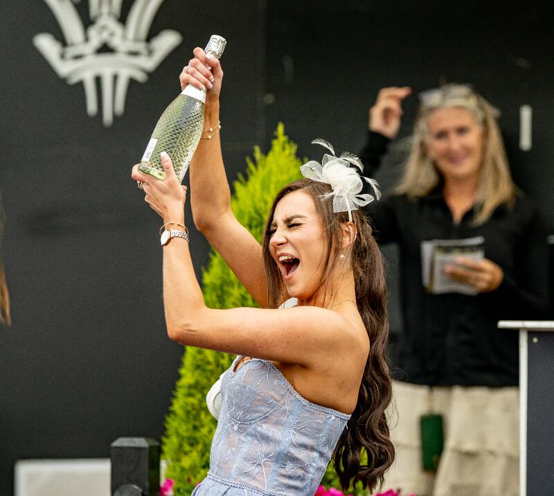 A race goer holding up a bottle of bubbly at Lingfield Park