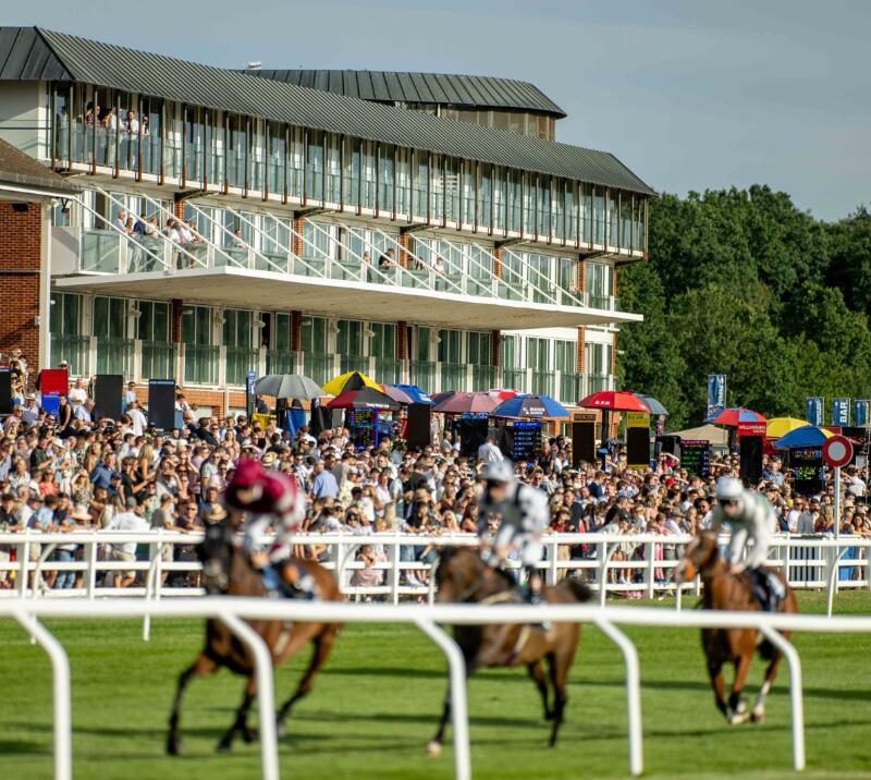 Horses racing past the grandstand and the betting stands at Lingfield Park